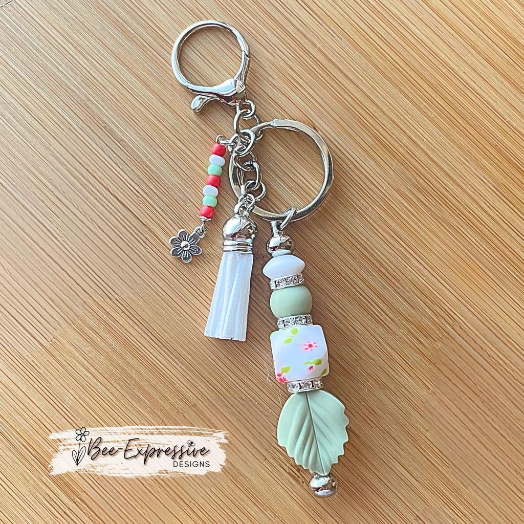 Beaded, handmade keychain with floral hexagon bead and silicone leaf! Lobster clasp, rhinestone spacers, beaded tassel with a flower charm!
